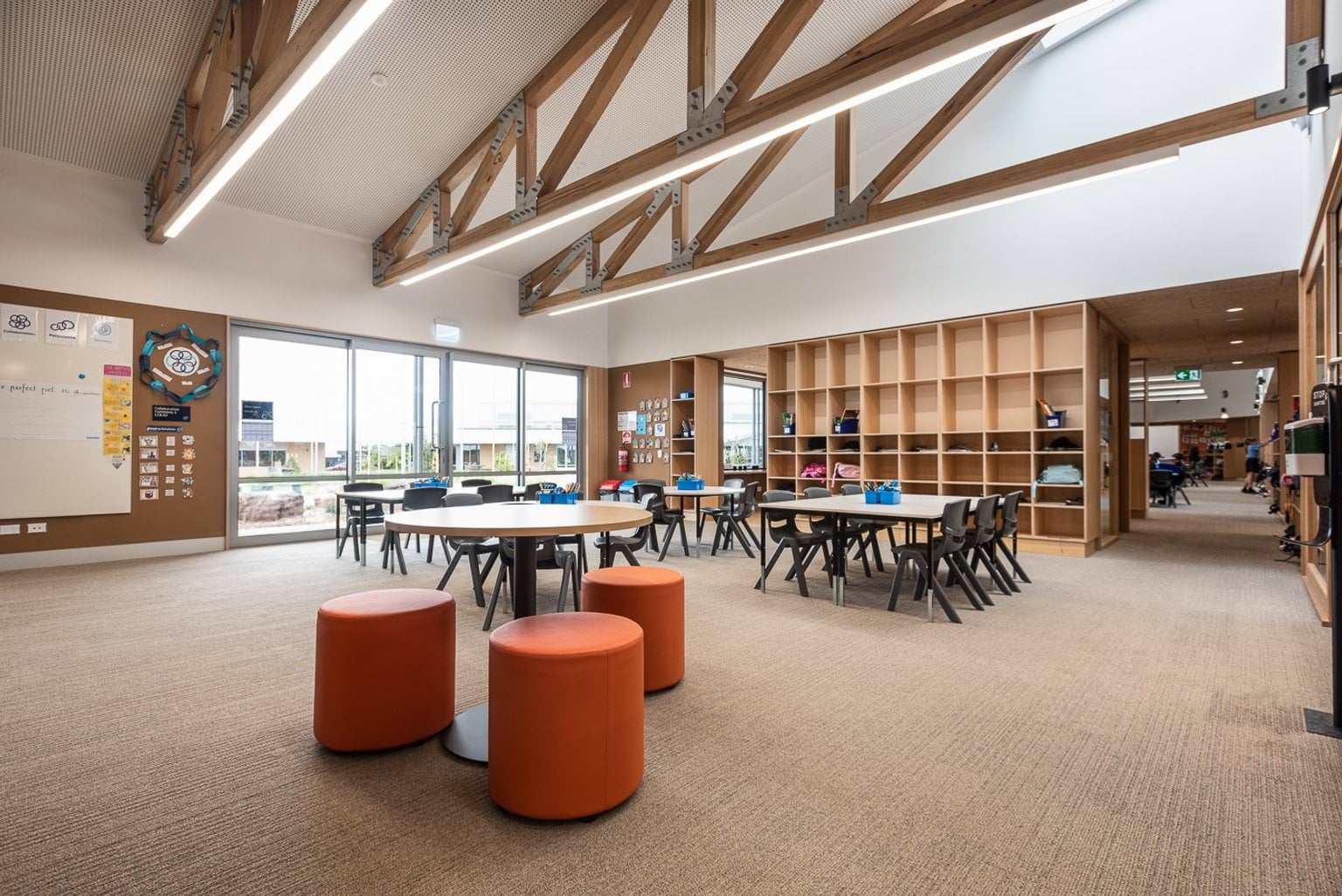 Open style classroom in a large room with two standard height square desks surrounded by chairs and one high desk with orange chairs. The space is bright and open.