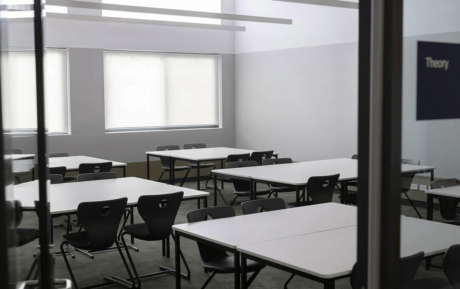 Classroom with 5 square desks, with 4 chairs around each desk.