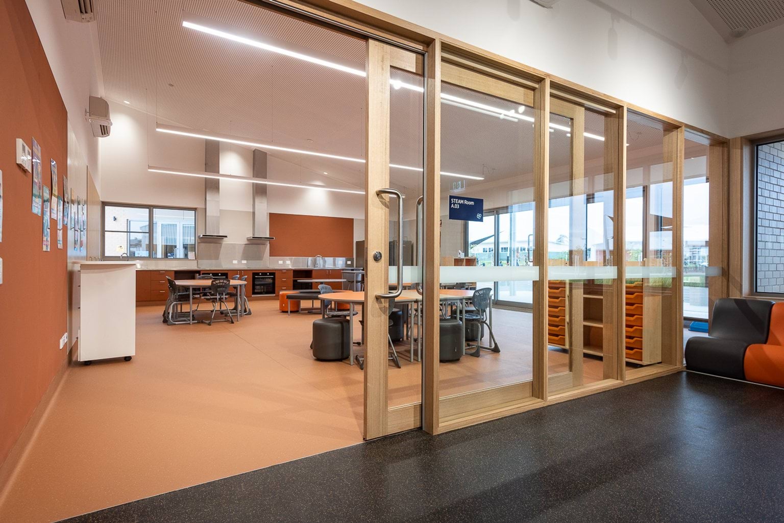 Orange classroom with sliding glass doors. The room has stainless steel benches at the back of the room for dedicated STEM activities and has circular desks throughout the room.